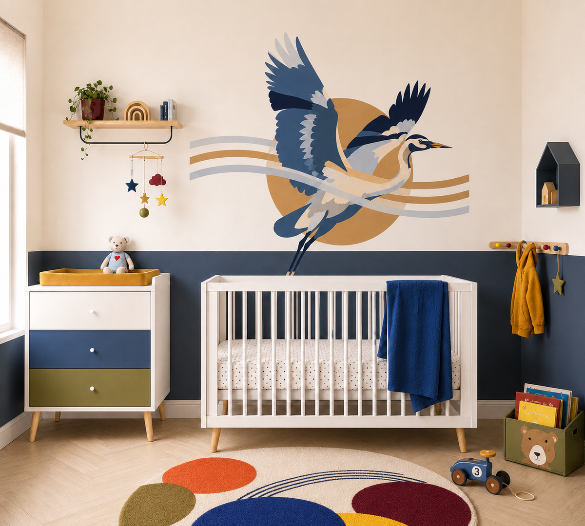 A styled nursery interior featuring a large wall decal of a blue and white heron bird flying over a tan sun on the wall above a white crib. The room has a cream and navy blue two-tone wall, a white dresser with blue and green drawers, and a colorful round rug on the light wood floor.